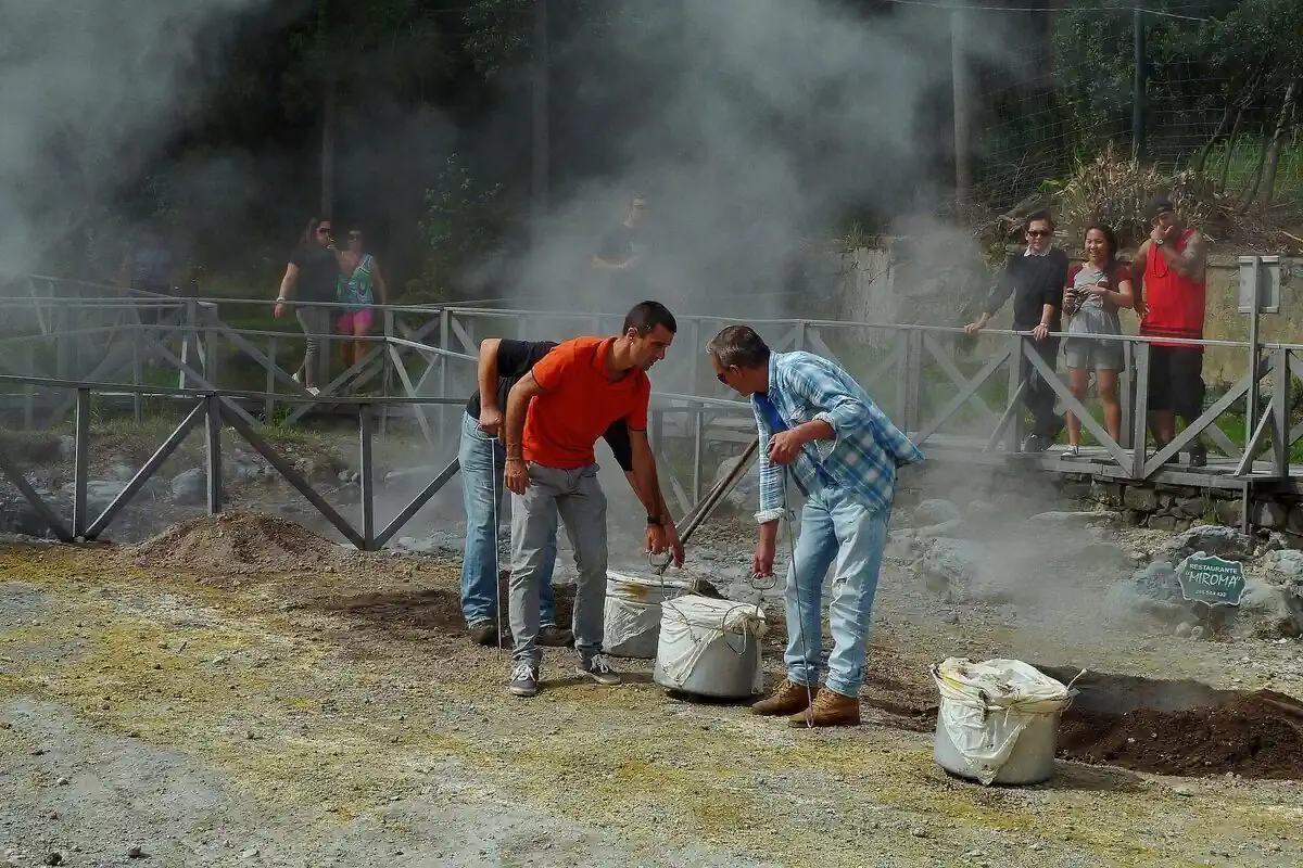 Cooks lifting pots of traditional Azorean cozido stew from steaming volcanic cooking holes in the ground